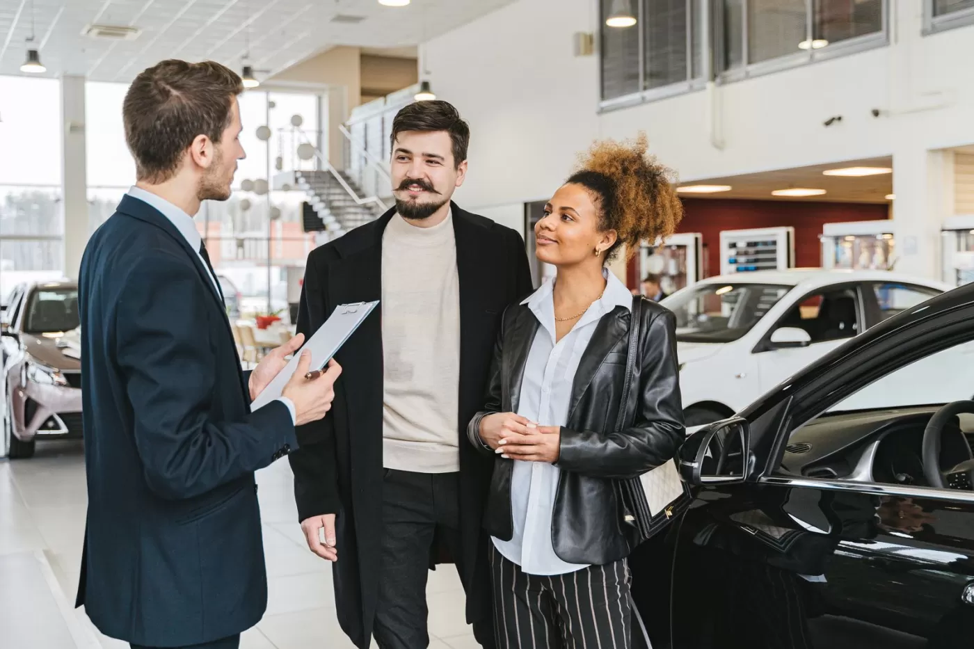 A salesperson and a colleague talking with a couple beside a car in a bright dealership